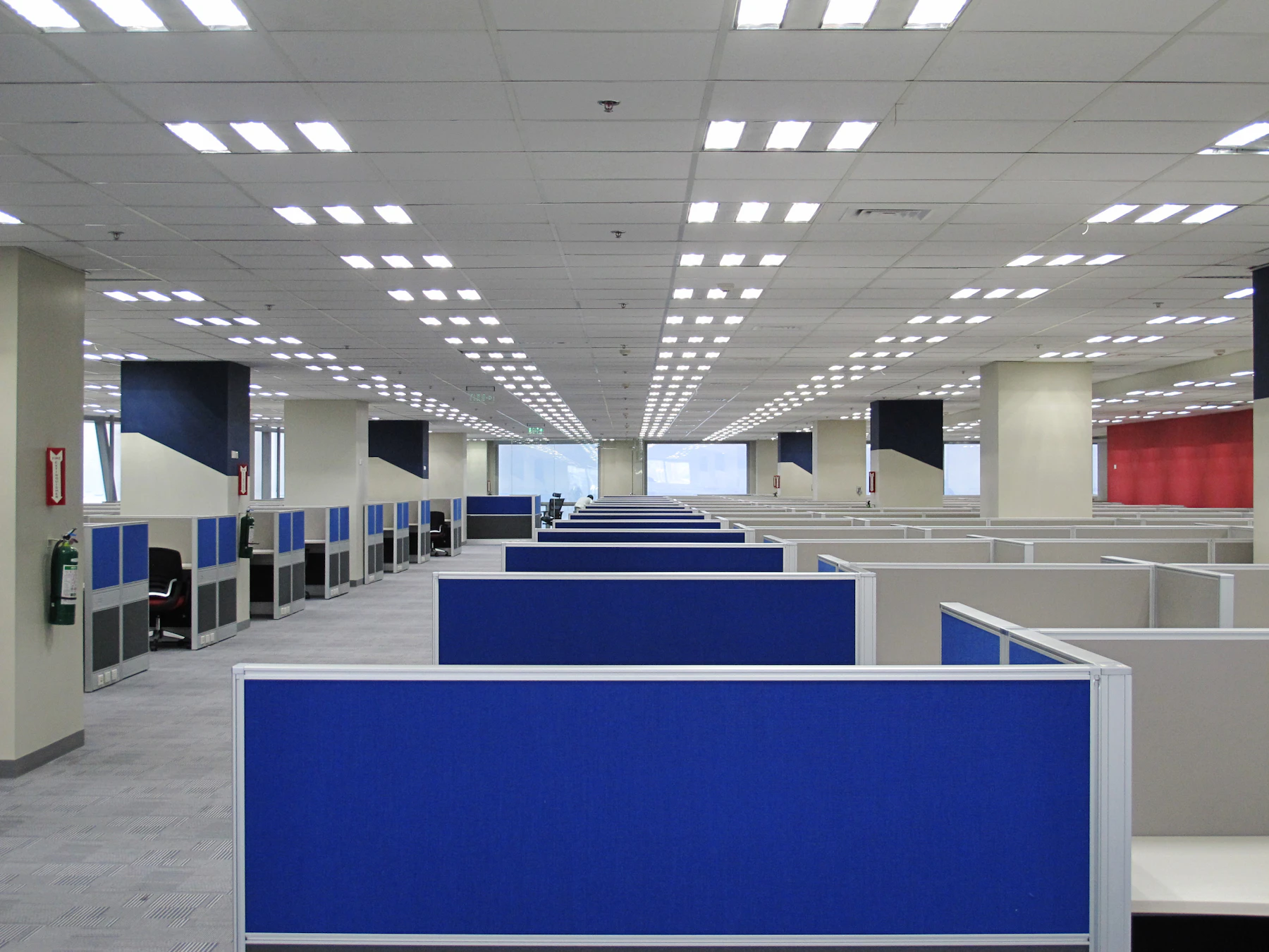 Empty open-plan office with rows of blue and white cubicles on carpeted floor