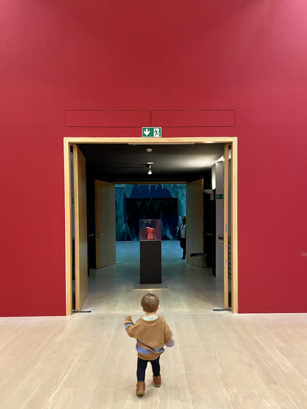 a little boy standing in a room with a red wall