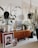 A cozy living room corner with a mid-century modern wooden sideboard featuring houseplants in various pots. Artworks are leaning against the cabinet, including a portrait and a family photo. A framed print with motivational text stands atop the sideboard, surrounded by stylish decor items such as a small lamp and a decorative container. The space is bright, with natural light coming through a window, and the overall decor exudes a homey and artistic vibe.