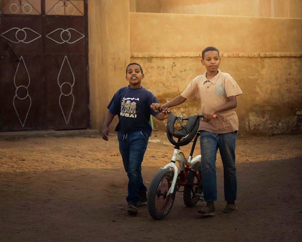 two young boys standing next to a bicycle