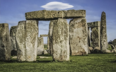 a stonehenge in a grassy field with a cloud in the sky