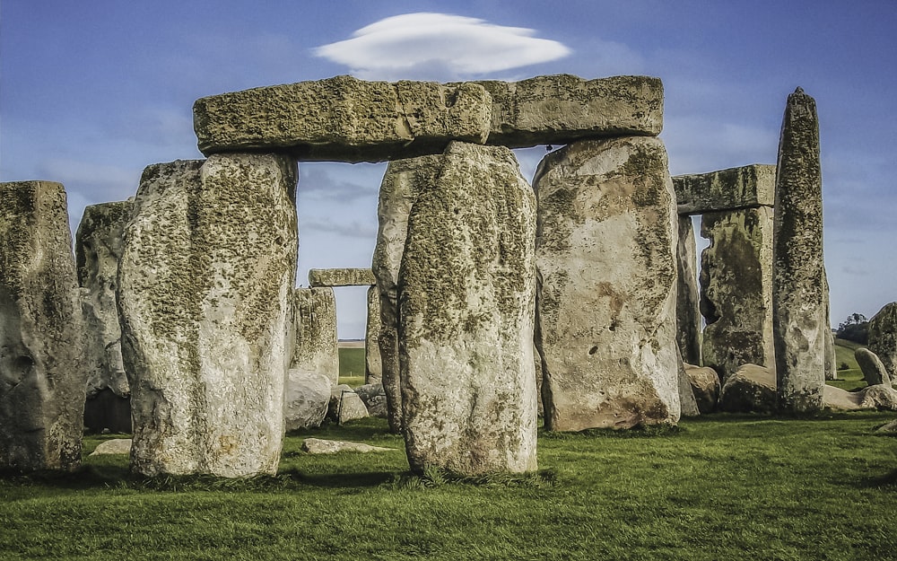 a stonehenge in a grassy field with a cloud in the sky