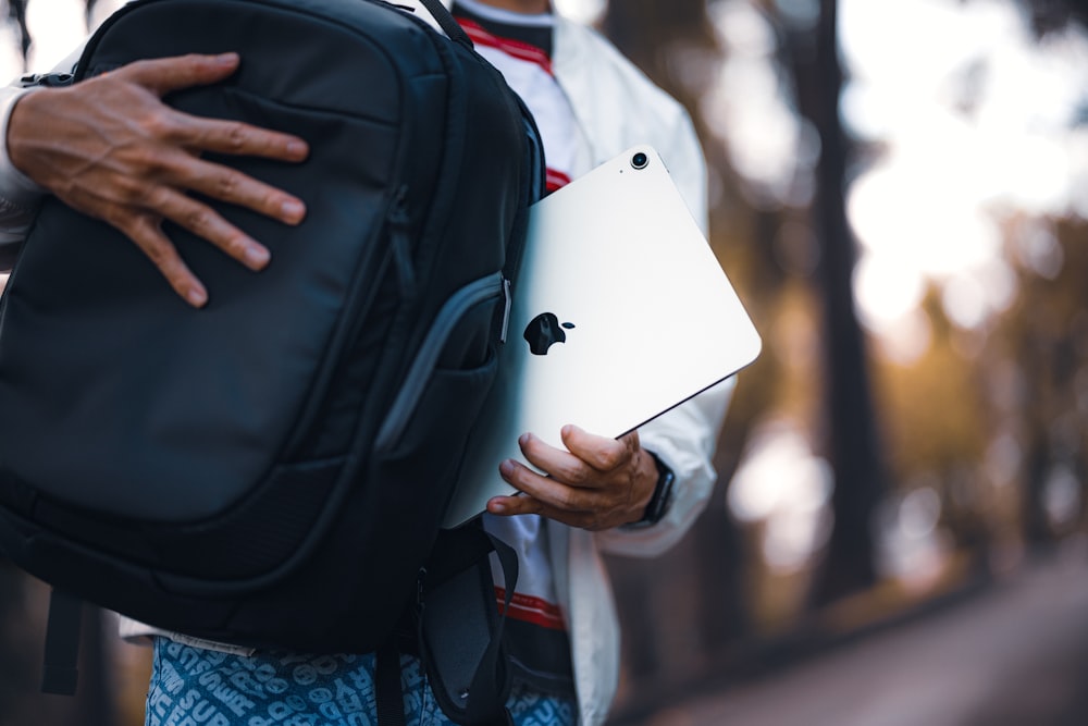 a man holding a laptop and a backpack