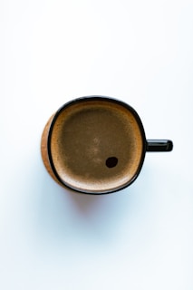 a brown cup with a black handle on a white surface