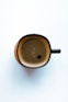 a brown cup with a black handle on a white surface