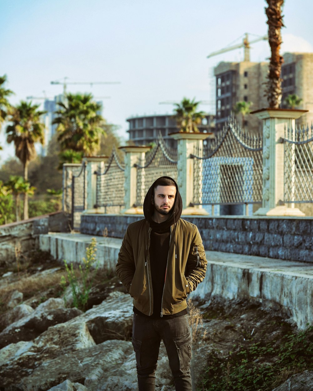 a man standing in front of a fence with his hands in his pockets