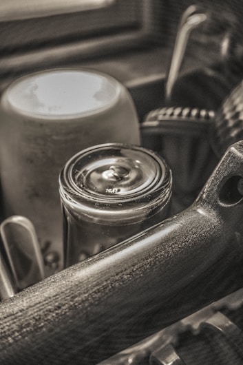 A close-up view of various dishes and utensils organized inside a dish rack, highlighting the smooth texture of a glass jar and a mug. The image is predominantly monochrome, creating a vintage, artistic atmosphere.
