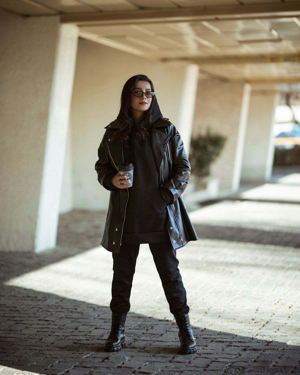 a woman in a black coat is standing on a sidewalk