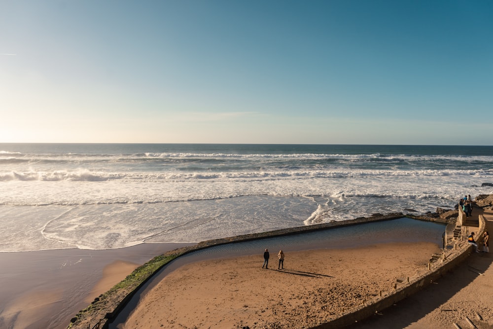 a couple of people standing on top of a sandy beach