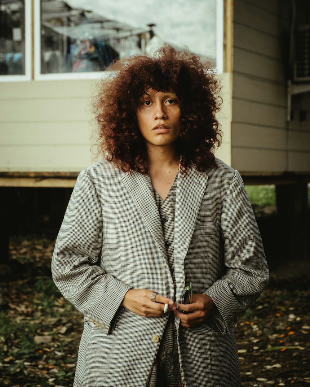 a woman with curly hair standing in front of a house