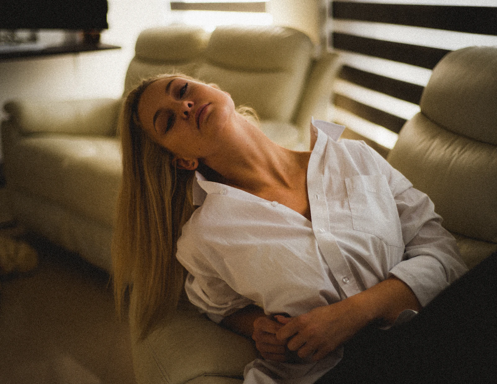 A woman in a white shirt resting on a couch with her head tipped back and her eyes closed.