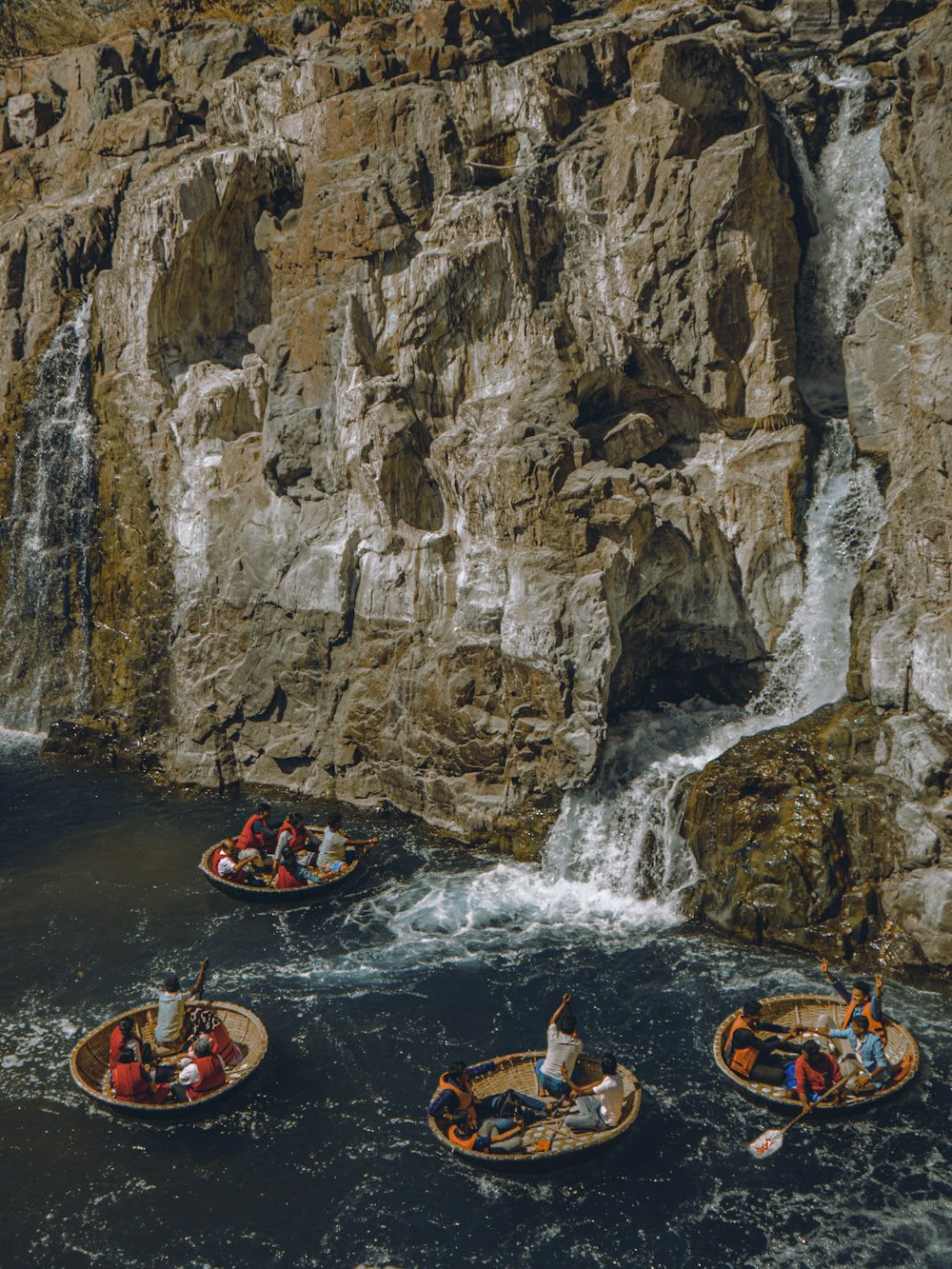 a group of people in small boats in front of a waterfall