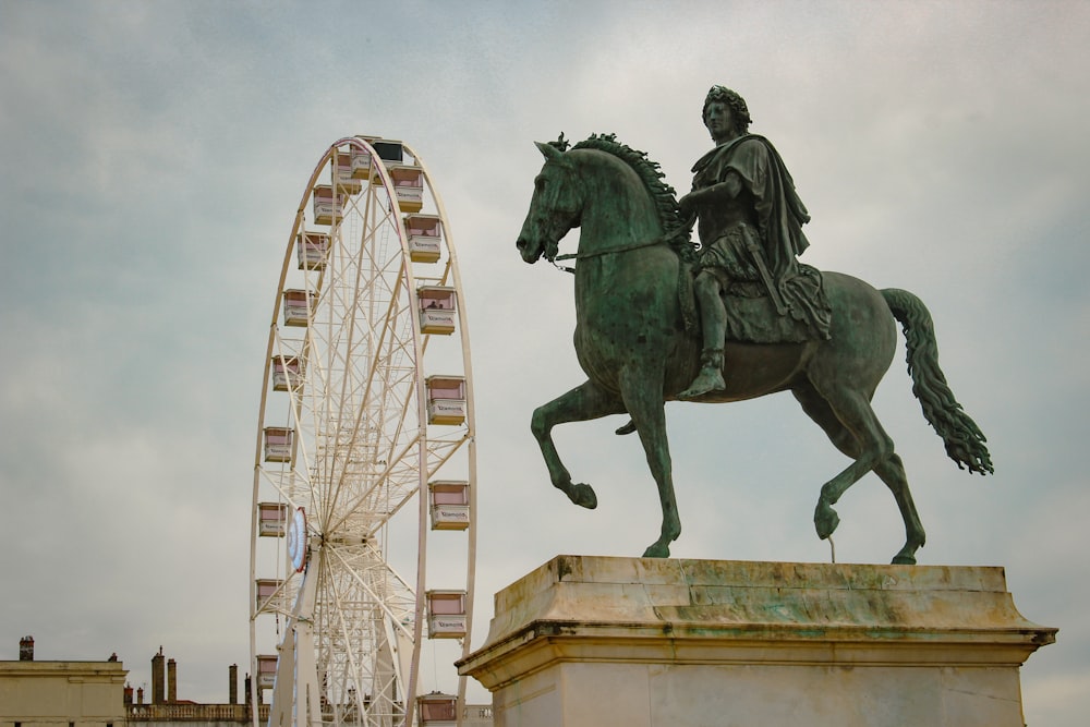 Una statua di un uomo che cavalca un cavallo accanto a una ruota panoramica