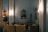 An elegant room furnished with vintage-style sofas and armchairs in a cozy arrangement. The walls are adorned with ornate mirrors and classic wall sconces, casting a warm glow. A display cabinet full of items is visible to the side, adding to the overall sophistication.