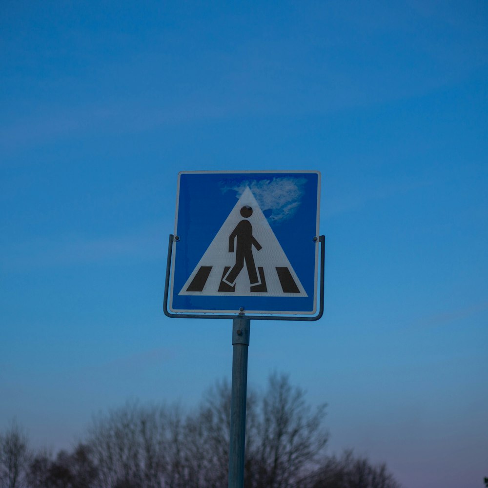 a blue and white pedestrian crossing sign with trees in the background