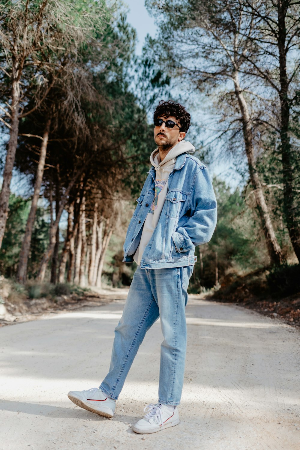 a man standing on a road wearing a denim jacket and jeans