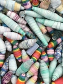 A collection of colorful, conical paper beads intricately rolled and arranged together. The beads display a variety of vibrant patterns and hues, ranging from pastel blues and pinks to bright multicolored stripes. The textures of the beads suggest a handmade, artisanal quality.
