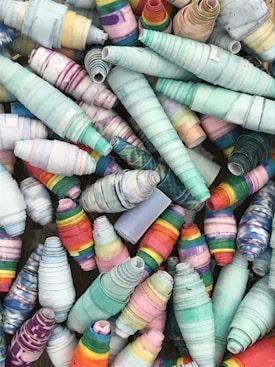A collection of colorful, conical paper beads intricately rolled and arranged together. The beads display a variety of vibrant patterns and hues, ranging from pastel blues and pinks to bright multicolored stripes. The textures of the beads suggest a handmade, artisanal quality.