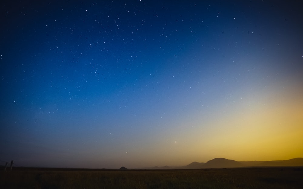 the night sky with stars above a field