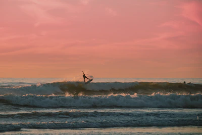 A surfer catching a wave at sunset with vibrant orange skies.
