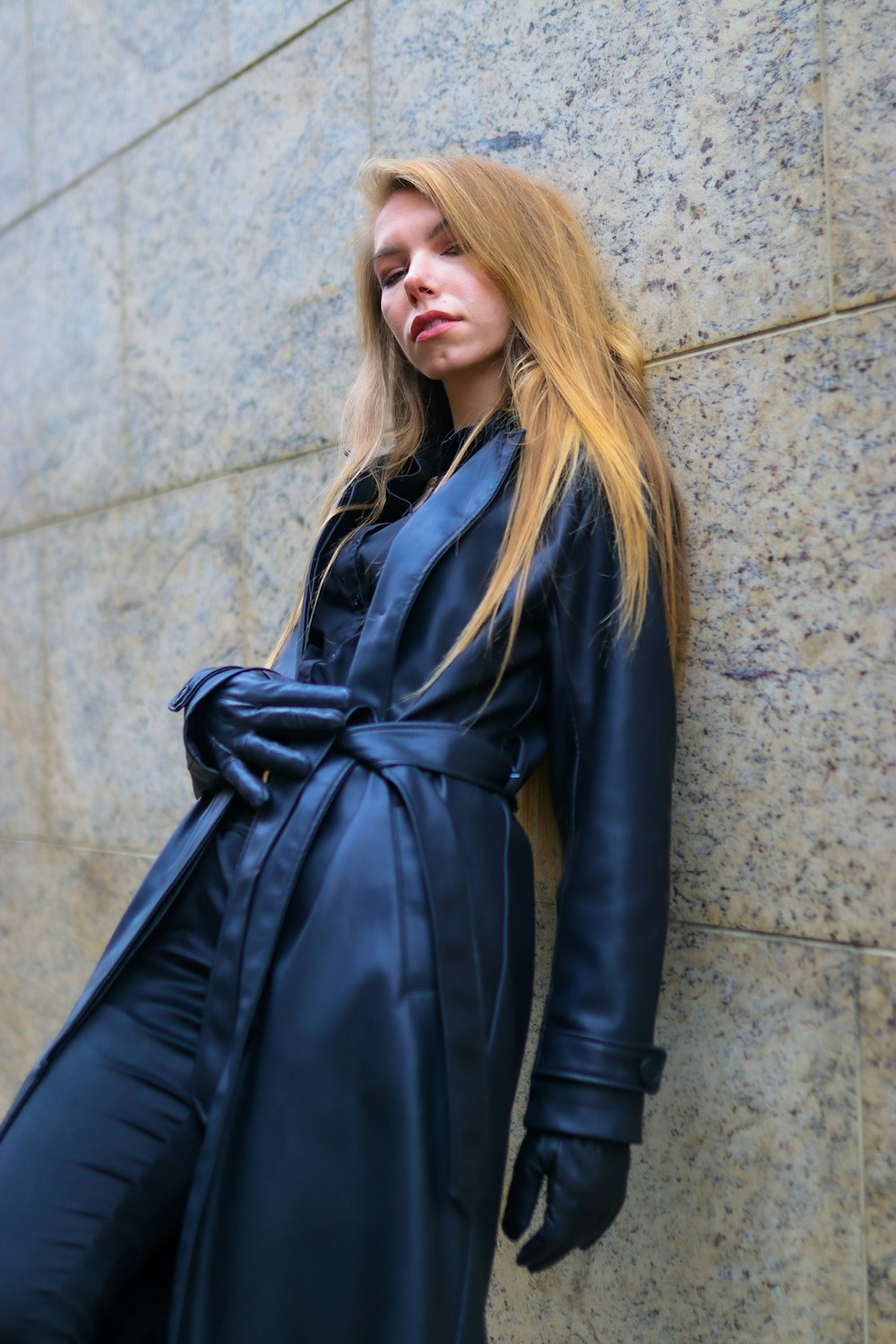 a woman leaning against a wall wearing a blue coat