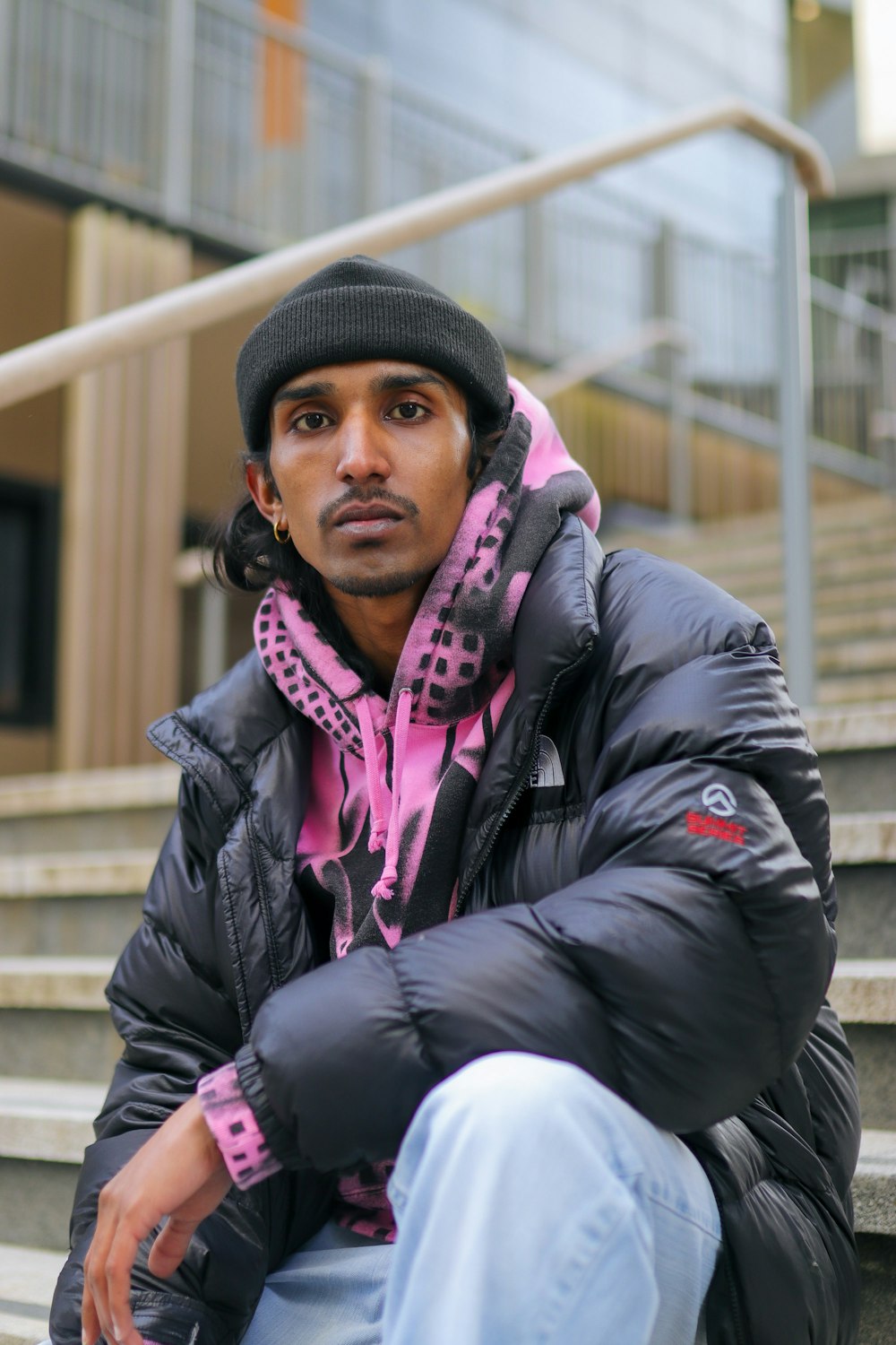 a man sitting on the steps wearing a black and pink jacket