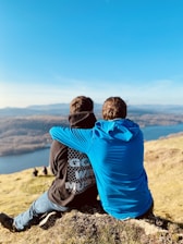 two people sitting on a hill overlooking a lake