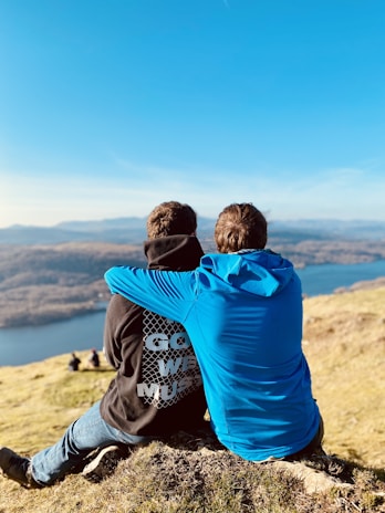 two people sitting on a hill overlooking a lake