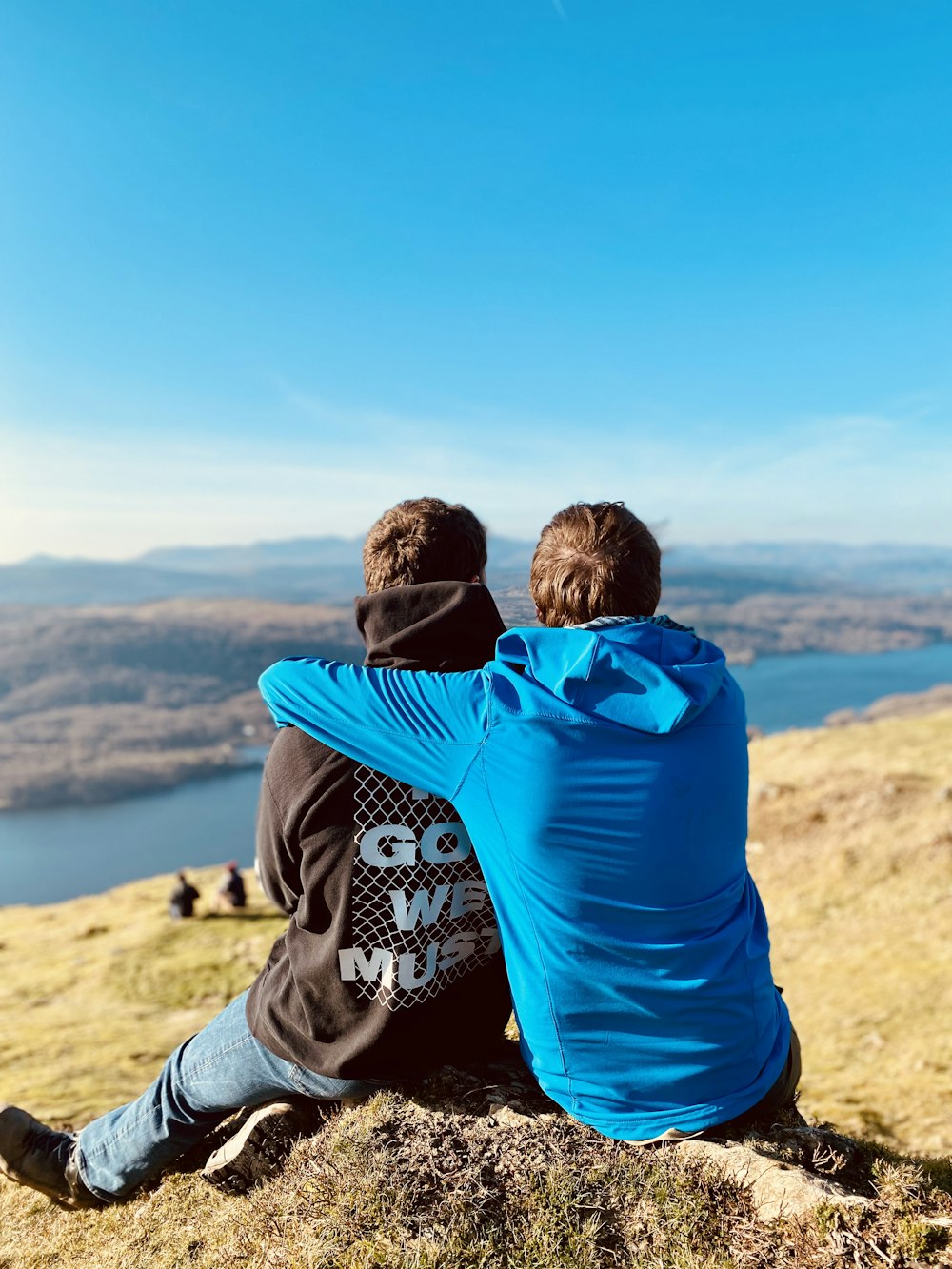 two people sitting on a hill overlooking a lake