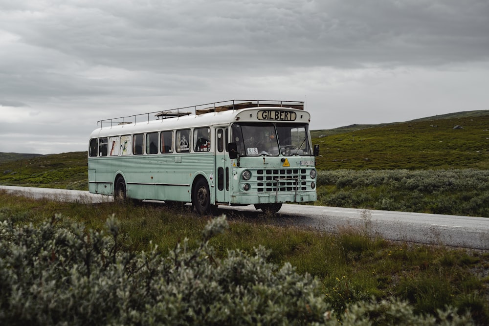 a blue bus driving down a road next to a lush green field