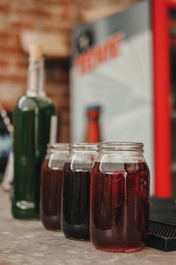 a table topped with jars of liquid next to a bottle of soda