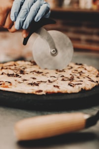 a person cutting a pizza with a pizza cutter