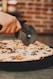 a person cutting a pizza with a pizza cutter