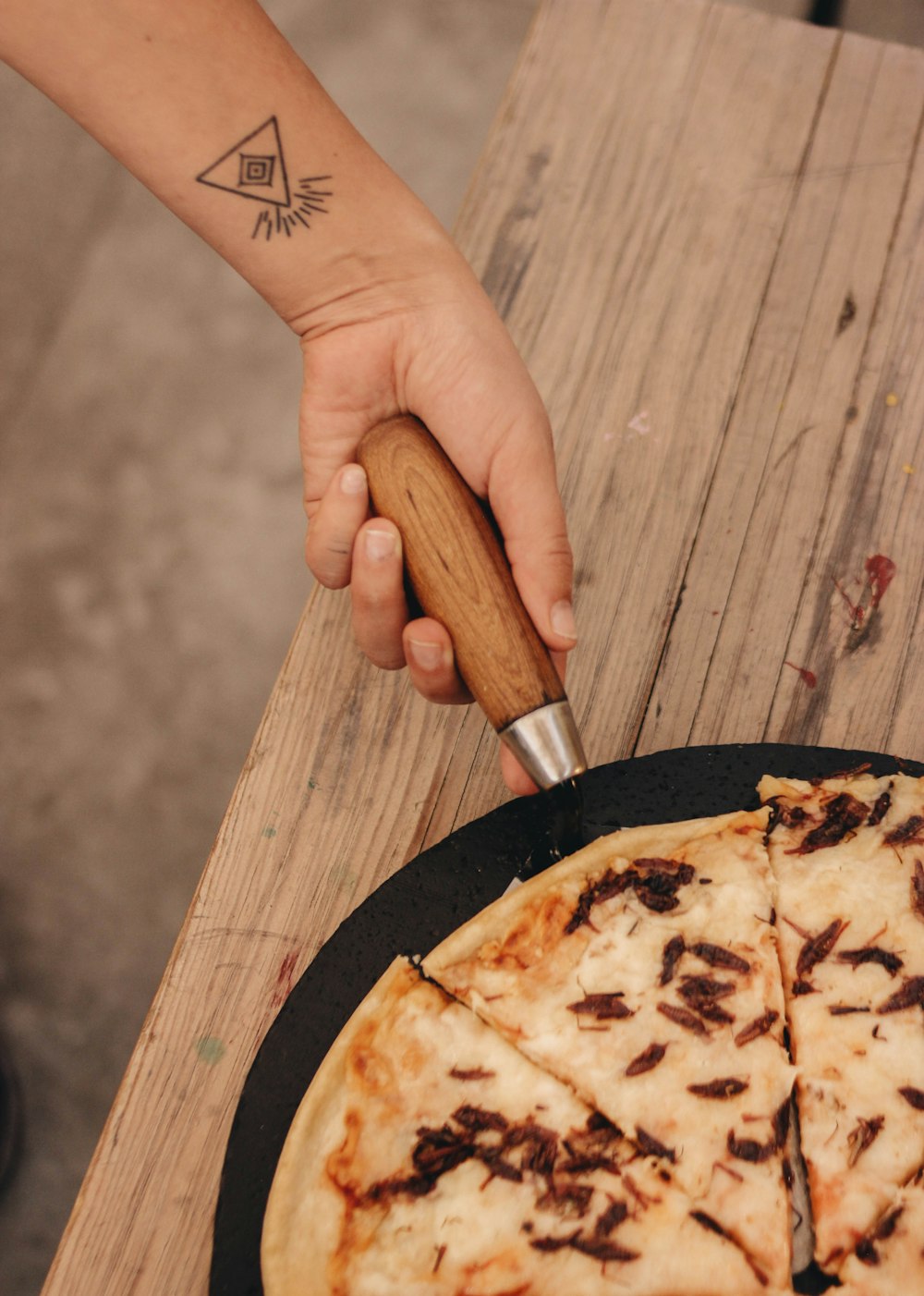 a person holding a pizza cutter over a pizza