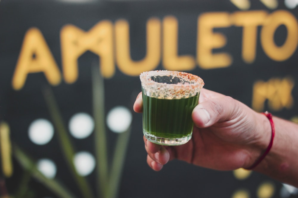 a person holding a green drink in front of a sign