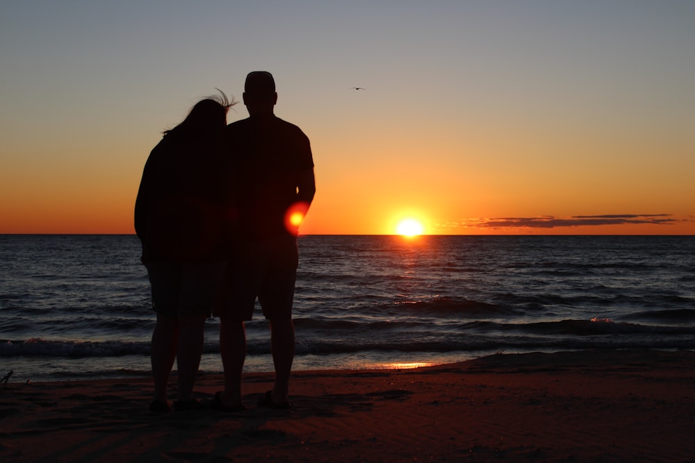 a man and a woman standing on a beach at sunset