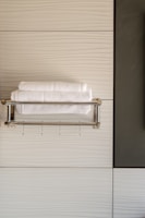 A modern bathroom scene with neatly folded white towels resting on a metallic towel rack against a textured, light-colored wall. The design features clean lines and a minimalist aesthetic.