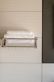 A modern bathroom scene with neatly folded white towels resting on a metallic towel rack against a textured, light-colored wall. The design features clean lines and a minimalist aesthetic.