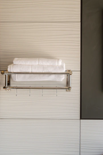 A sleek stainless steel wall-mounted towel rack holding neatly folded towels in a bright bathroom.