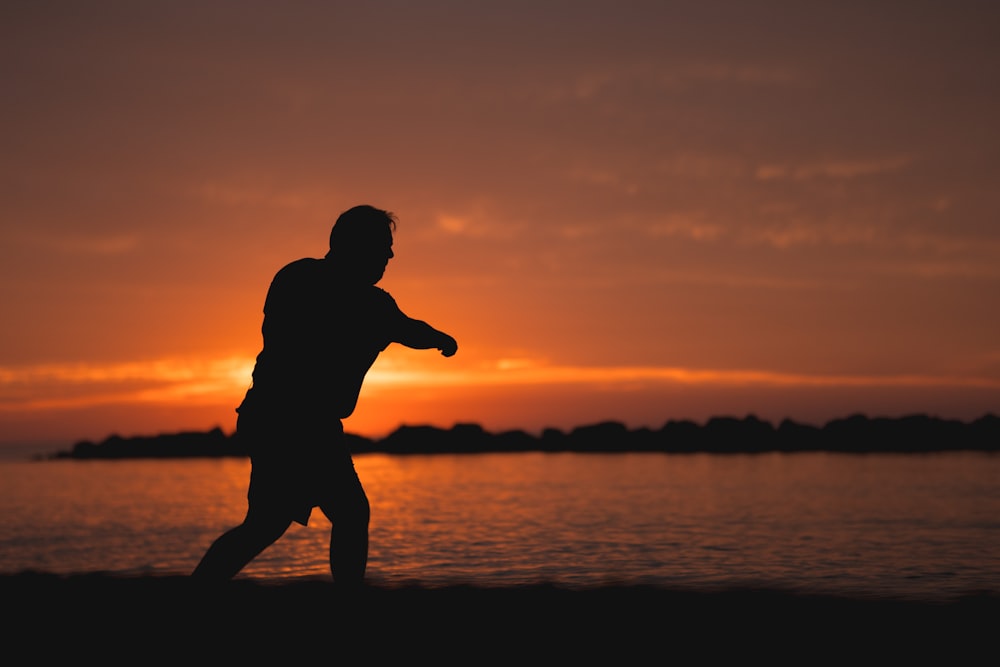 Silhouette d’un homme lançant un frisbee au coucher du soleil