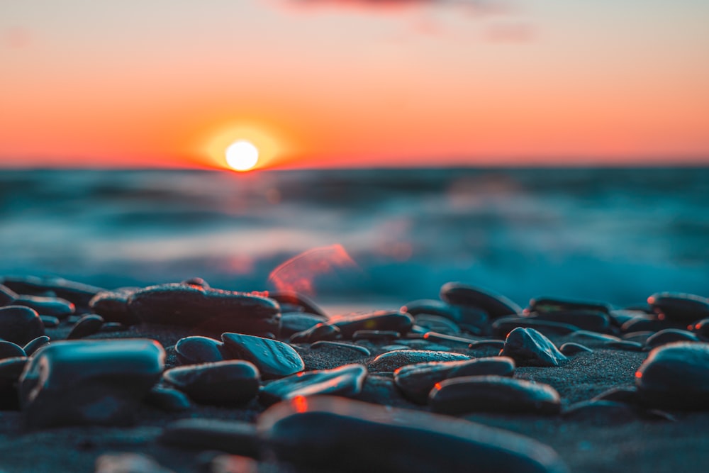 the sun is setting over the ocean and rocks