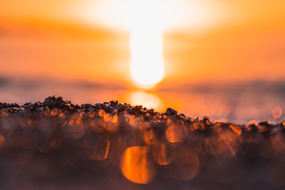 the sun is setting over the ocean with small rocks in the foreground