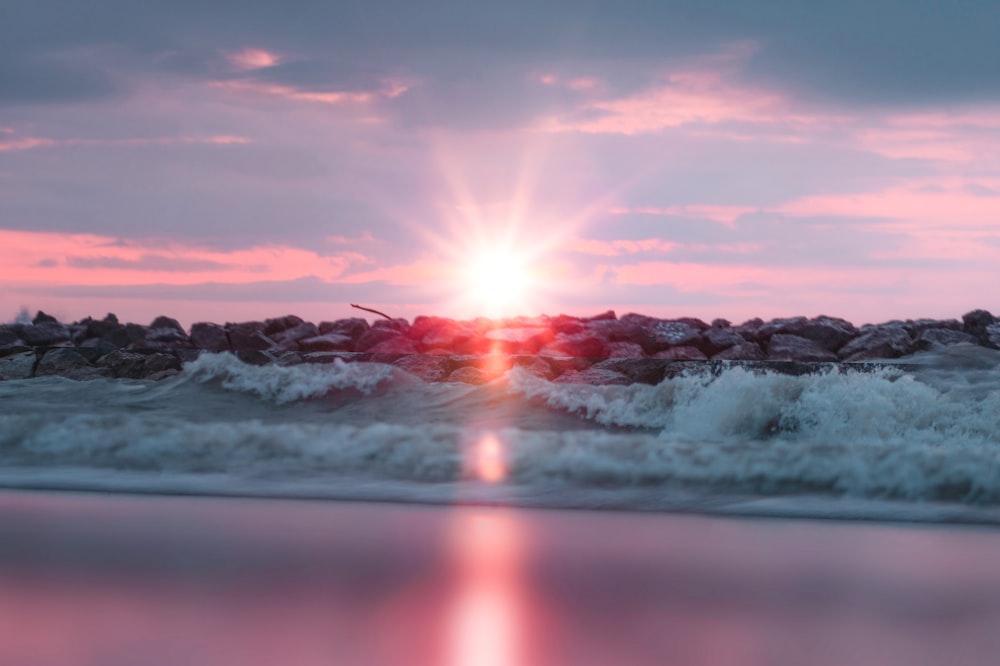 the sun is setting over the water and rocks