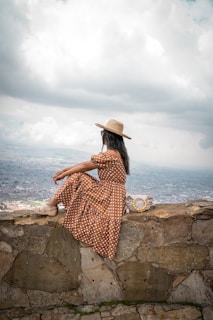 a woman in a dress and hat sitting on a stone wall