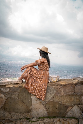 a woman in a dress and hat sitting on a stone wall