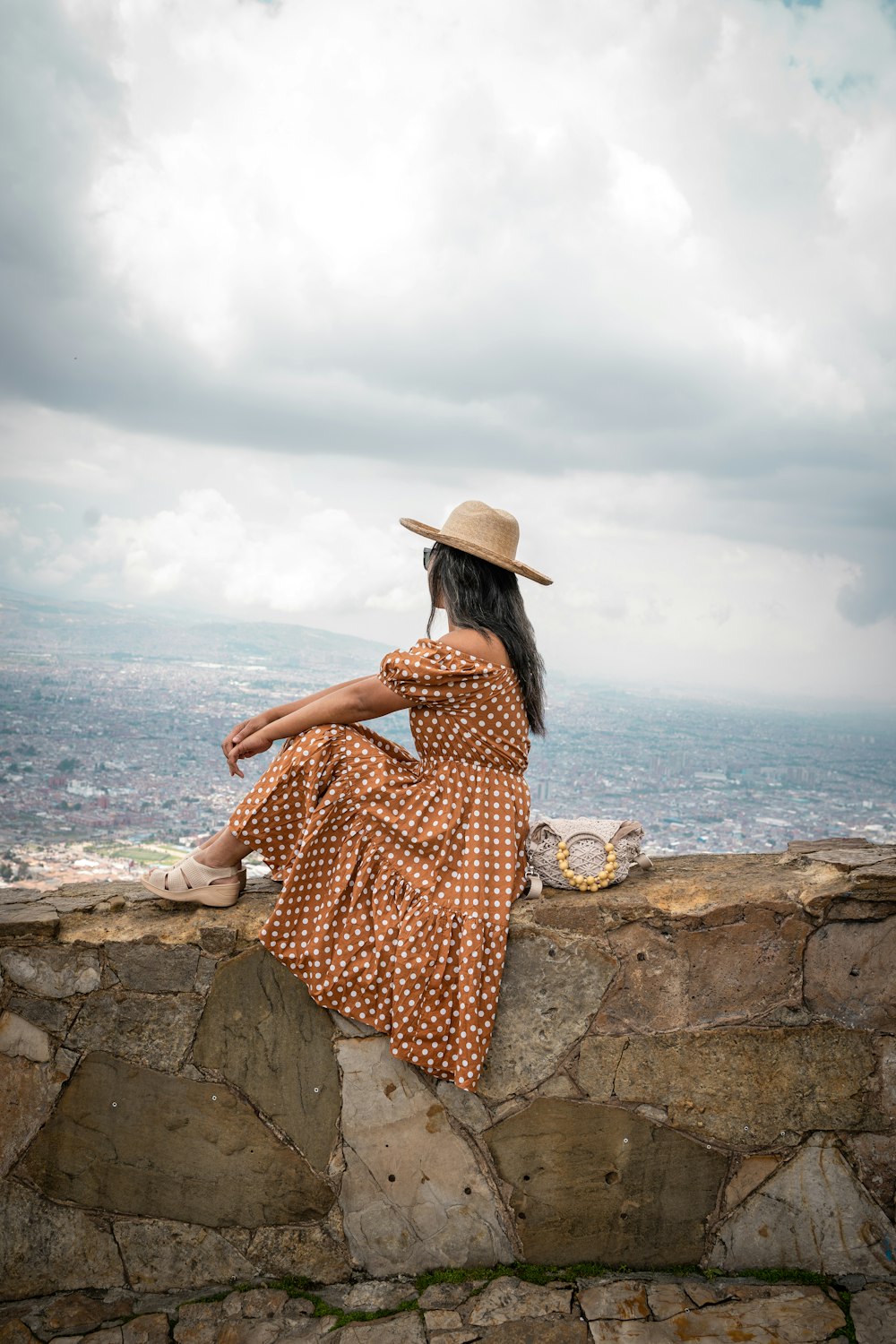 a woman in a dress and hat sitting on a stone wall