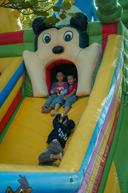 A tall inflatable water slide with children sliding down and splashing into a pool