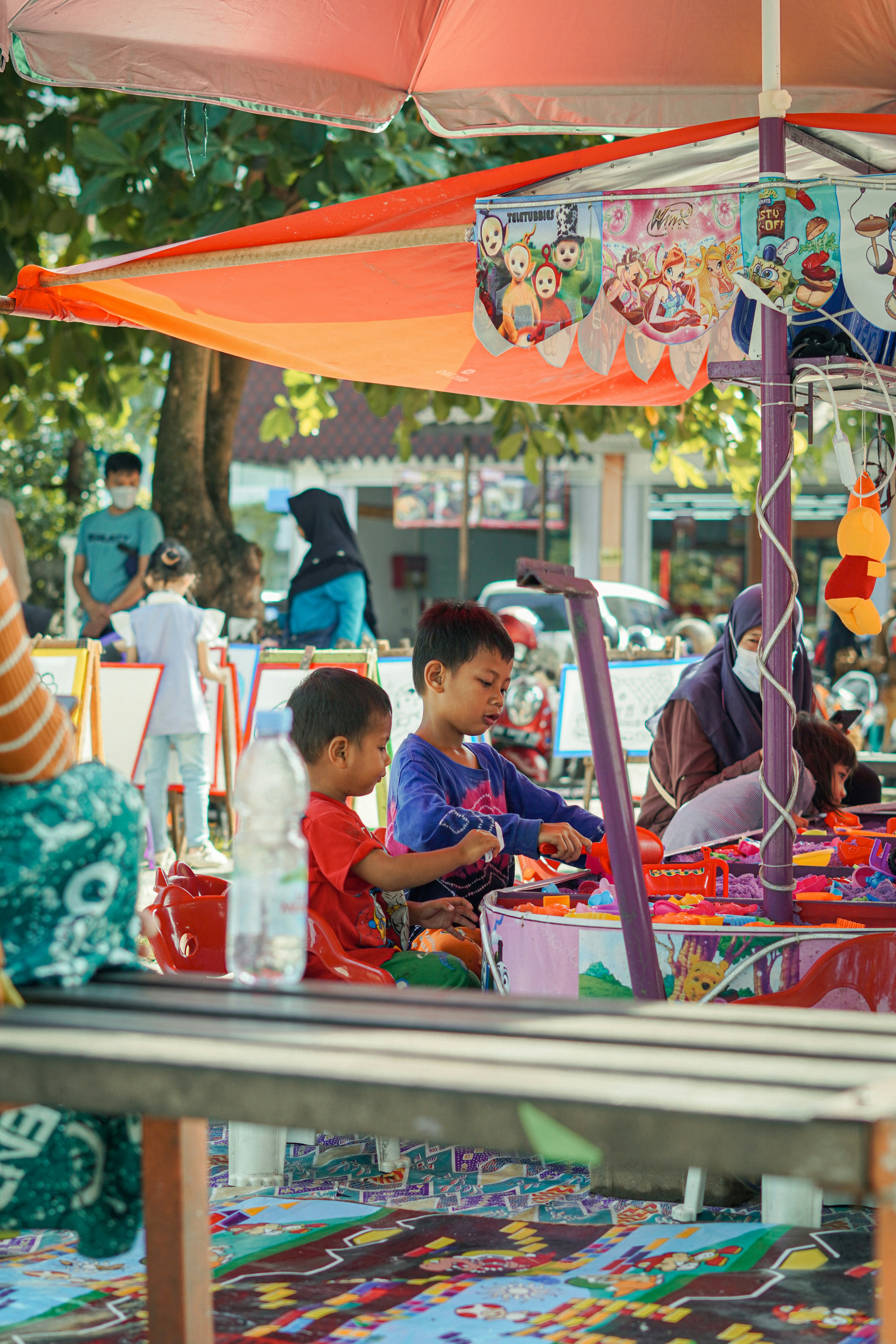 a group of children sitting under a colorful umbrella