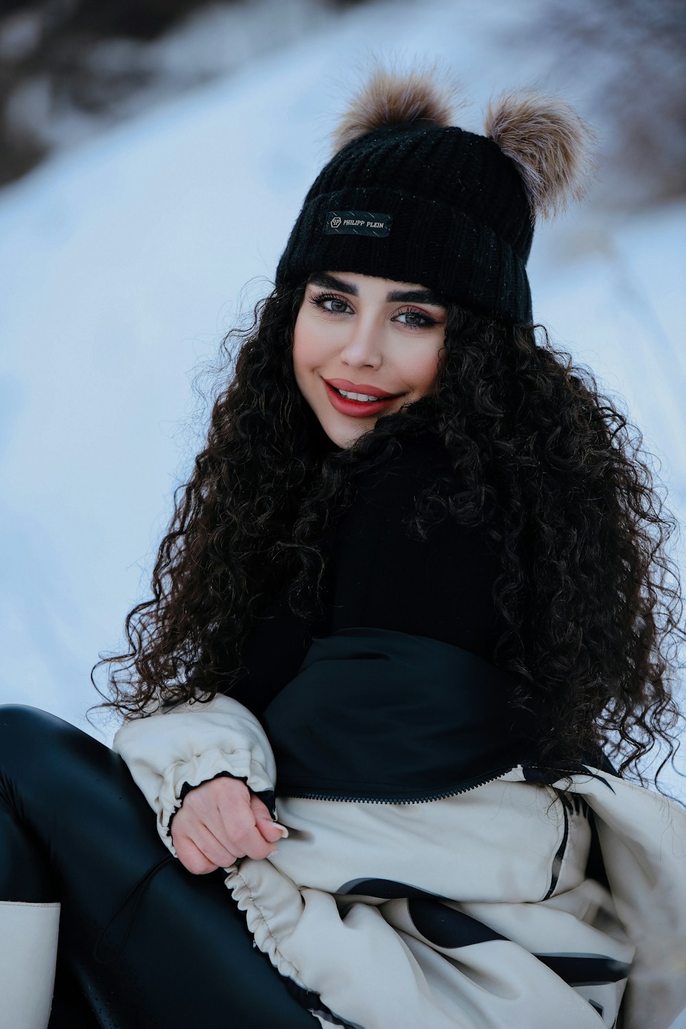 a woman sitting in the snow wearing a black hat