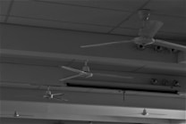 Several ceiling fans are mounted on a ceiling with a grid-like pattern. The environment appears functional, possibly an office or lecture hall. The image is in black and white, giving it a stark appearance.